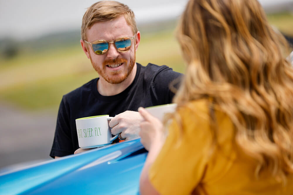 A fellow with a mug of tea, discussing important matters over the nose of an airplane.